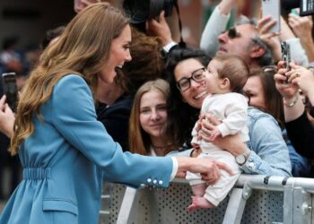 Kate Middleton smiling as she tickles a baby