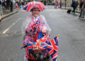 A man riding a mobility scooter covered in Union flags. He has a small umbrella attached to his hat, which also has a Union flag design.