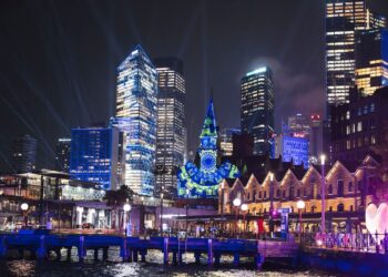 A light projection shines on the clock tower and sydney city skyline.