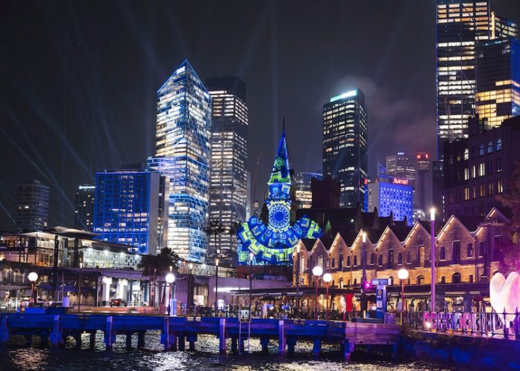 A light projection shines on the clock tower and sydney city skyline.