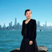 A young smiling Asian woman stands before a body of water with the San Francisco skyline in the background