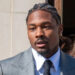 Stefon Diggs, in a gray suit and black tie, is walking outside with a woman in the background.