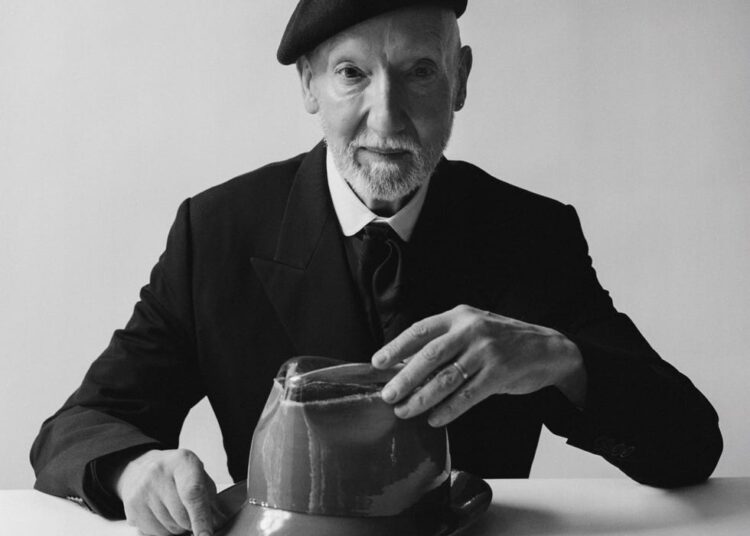 A person in formal attire examining a hat on a table.
