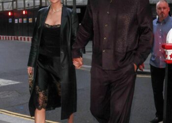 A couple walking hand in hand down a city street during the evening.