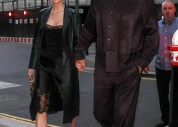 A couple walking hand in hand down a city street during the evening.