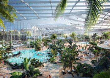 Therme Manchester indoor water park with large pools, palm trees, and people enjoying leisure activities.