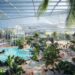 Therme Manchester indoor water park with large pools, palm trees, and people enjoying leisure activities.