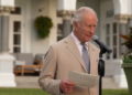 King Charles wears a pale jacket and tie as he stands in a beautifully manicured garden in Bermuda