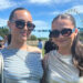 Two young women in sunglasses smile at the camera on a music festival site.