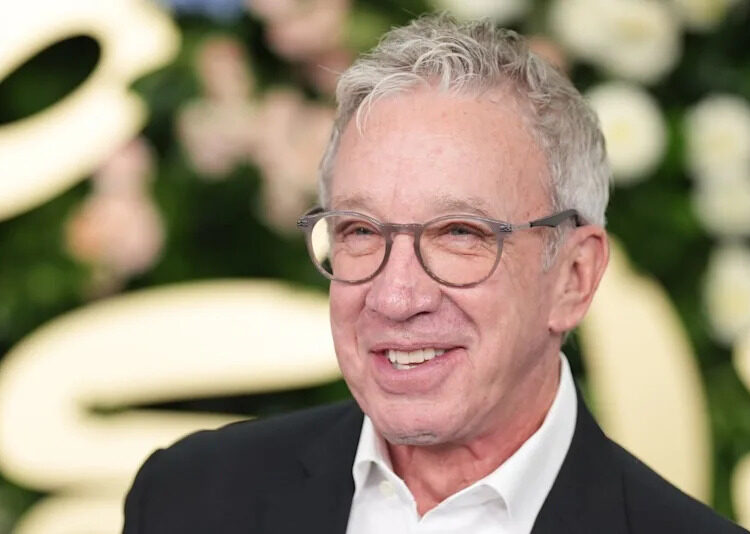 Tim Allen smiling, wearing glasses and a suit, in front of a floral backdrop.