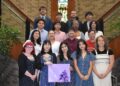 Group of students pose on an indoor staircase in a brick building, with stained-glass windows behind them and one person holding a purple gift bag.