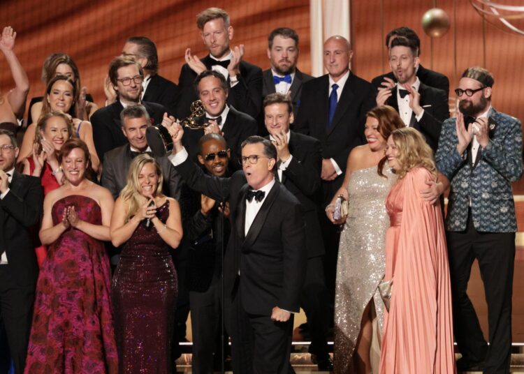 Stephen Colbert, in front of a crowd in formal wear, holds his Emmy statuette.