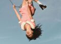 Olivia Rodrigo in a pink collared dress on a swing in the air.