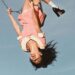 Olivia Rodrigo in a pink collared dress on a swing in the air.