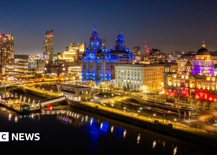 A night city scape of Liverpool lit up in different colours looking out over the docks.