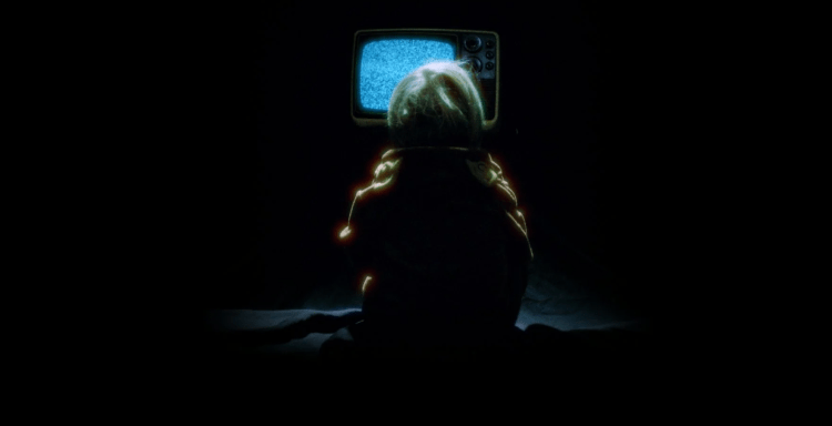 A person sits in the dark in front of a TV looking into the static.