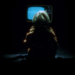 A person sits in the dark in front of a TV looking into the static.