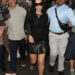 Charli XCX walks down the street in London wearing a black leather miniskirt with black pointed-toe heels and a sheer black top.
