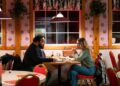 Maria Bakalova and Zach Cherry sit in a restaurant in a still from