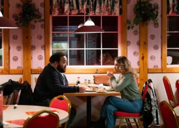 Maria Bakalova and Zach Cherry sit in a restaurant in a still from