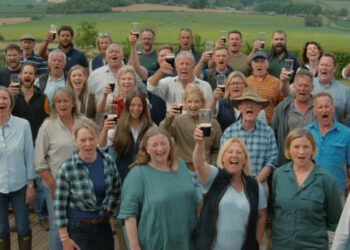 The choir is standing outside and looking at the camera, many toasting the picture with a pint. There are men and women with Jeremy Clarkson in the middle.