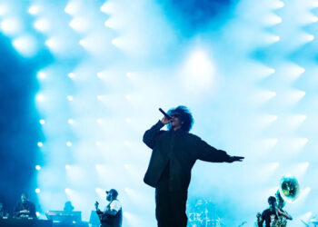 Jay-z on stage with bright blue lights in the background, musicians playing instruments on the side. This was at Roots Picnic 2026