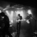 Band performs on stage with stark spotlighting.