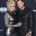 Bunnie Xo, in a black latex dress, and Jelly Roll, in a black suit with face and arm tattoos, pose together at the 68th GRAMMY Awards Pre-GRAMMY Gala.