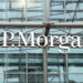 The image shows the J.P. Morgan logo on a glass building facade with metal framework.