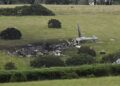 A picture of the wreckage shows debris strewn across the field where the helicopter crashed