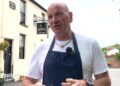 A restaurant owner wearing a navy blue apron and white t-shirt stands outside his restaurant while explaining the impact traffic will have on his business