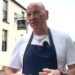 A restaurant owner wearing a navy blue apron and white t-shirt stands outside his restaurant while explaining the impact traffic will have on his business