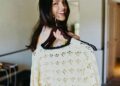 Person smiling while holding a cream crochet sweater on a hanger.