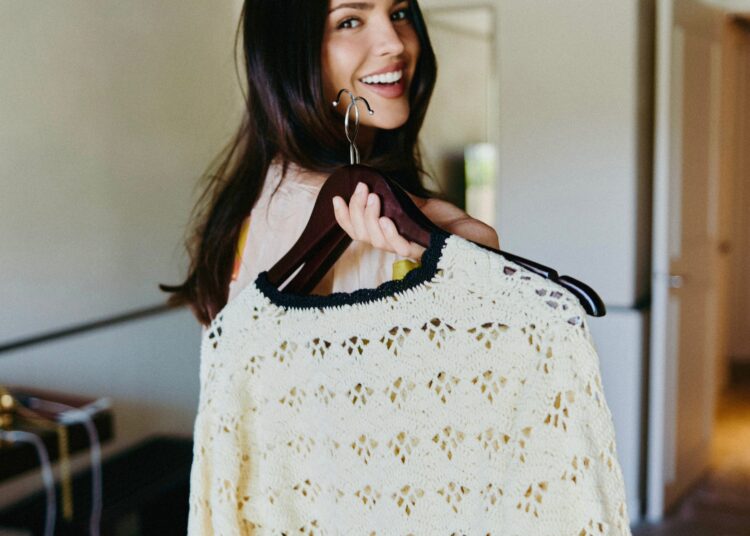 Person smiling while holding a cream crochet sweater on a hanger.