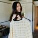 Person smiling while holding a cream crochet sweater on a hanger.