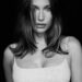 Black and white portrait of Hailey Bieber with long hair, wearing a light-colored tank top, looking directly at the camera.