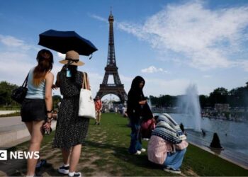 people under an umbrella because of the heat in paris with the Eiffel Tower in the background