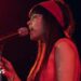 Lily Allen wearing a red dress and head scarf singing into a microphone in a dark chapel