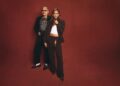 Two people in stylish outfits against a red backdrop.