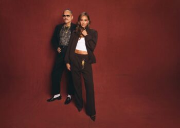 Two people in stylish outfits against a red backdrop.