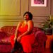 Full body of barefoot plump African American female laughing with mouth opened sitting on comfortable sofa