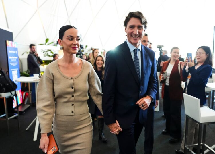 A man and woman hold hands while walking through a crowd.