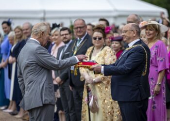 King Charles, in a grey suit, lays his hands on a red velvet cushion carrying the keys of the City of Edinburgh