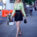 Person walking on a city sidewalk in a stylish outfit with a smile.