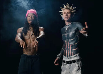 Wiz Khalifa with a pink beanie and dreadlocks, mgk shirtless with spiky hair and tattoos, wearing camo pants.