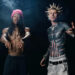 Wiz Khalifa with a pink beanie and dreadlocks, mgk shirtless with spiky hair and tattoos, wearing camo pants.