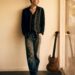 Man leaning against a wall next to a guitar.