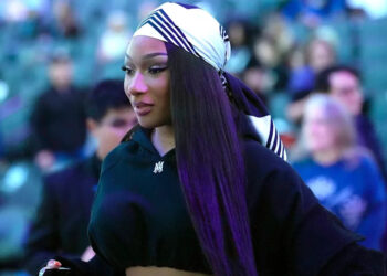 Megan Thee Stallion wearing a black outfit and a striped headscarf, walking in a crowd.