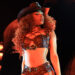 Megan Thee Stallion in a cowboy hat and leather outfit on stage, with dramatic lighting and a dynamic pose.
