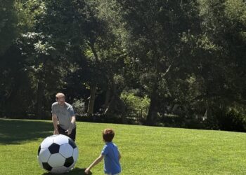 Two people playing with a giant soccer ball on a grassy field.